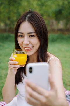 美丽的亚洲女旅行家用橙汁自拍的肖像。