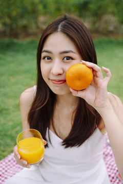 美丽的亚洲旅行家妇女在户外拿着橘子水果和果汁的肖像。
