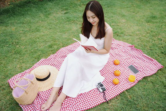 穿着白色连衣裙的美丽亚洲女人在公园户外看书。