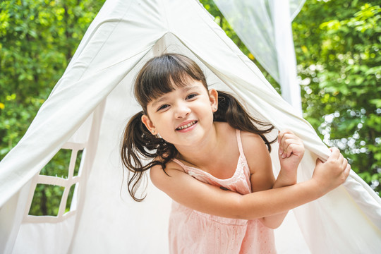 亚洲可爱的小女孩喜欢呆在花园里的白色露营帐篷里。