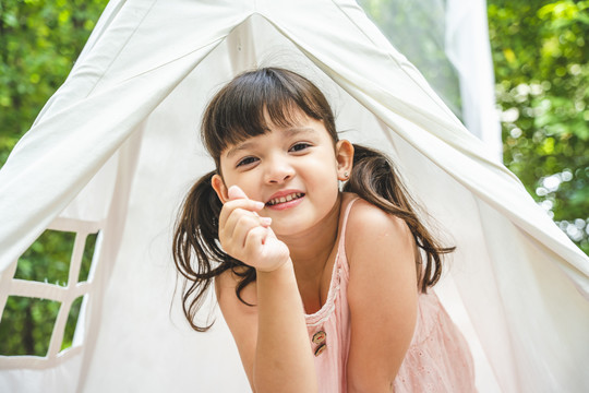 亚洲可爱的小女孩喜欢呆在花园里的白色露营帐篷里。