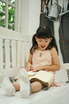 亚洲小女孩带着幸福的表情在白色长椅上看书。