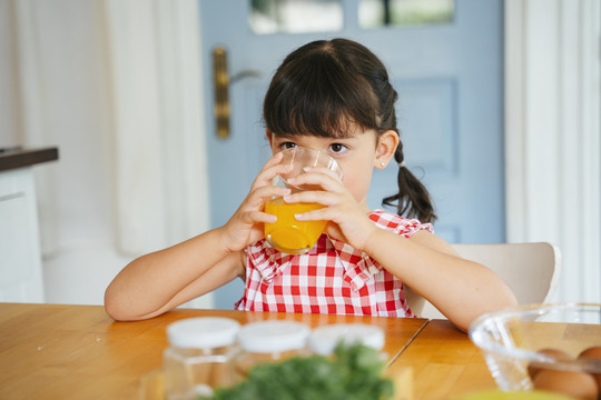 亚洲小孩在厨房里喝橙汁。