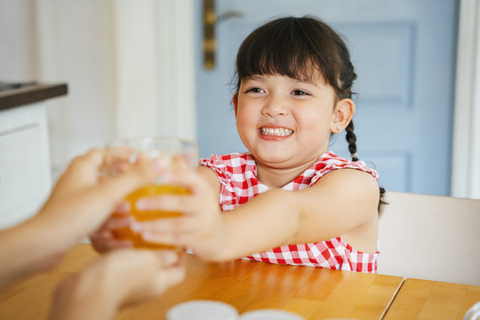 亚洲小女孩从妈妈手里拿着一杯橙汁。