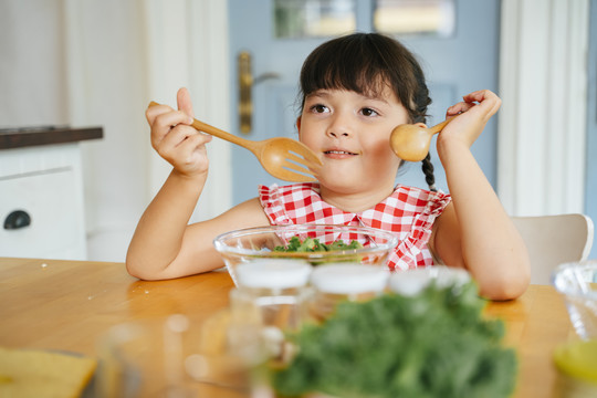亚洲小孩在厨房用木勺和叉子吃沙拉碗。