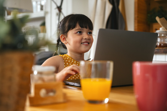 亚洲小女孩在家里的桌子上使用笔记本电脑。