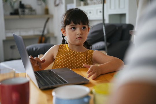 亚洲小女孩在笔记本电脑上做作业，并请妈妈帮助她。