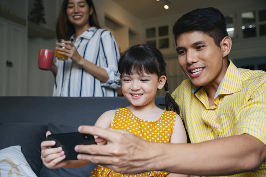 亚裔父亲教女儿如何玩手机游戏。
