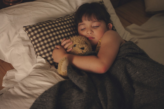 亚洲小孩晚上在床上睡觉和拥抱泰迪熊。