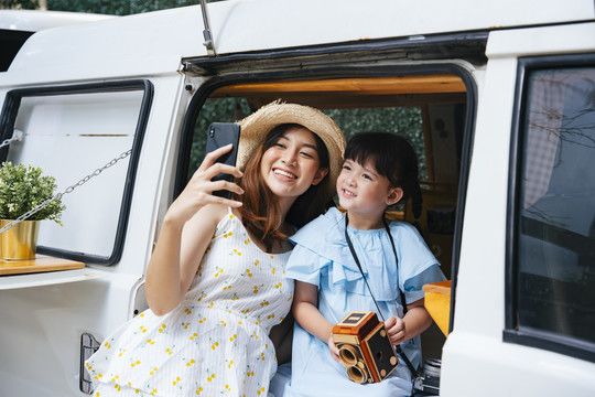 亚洲母亲和孩子在娱乐车家用车上用智能手机自拍。