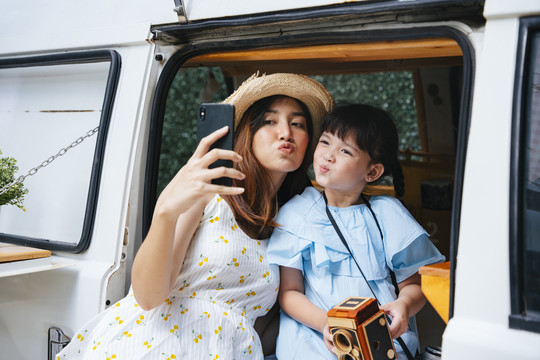 亚洲母亲和孩子在娱乐车家用车上用智能手机自拍。