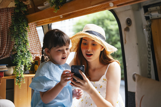 亚洲母亲和孩子在休闲车内看着智能手机屏幕截图。