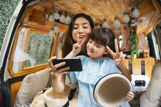 亚洲母亲和孩子在房车行李箱用智能手机自拍，玩得很开心。