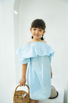 身着浅蓝色连衣裙的亚洲儿童的肖像，白色背景上拿着木篮子。