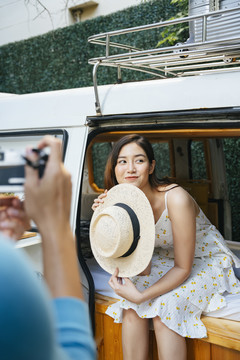 一对亚洲夫妇站在一辆汽车旁，在一辆休闲车内拍照。