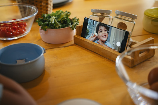 孩子在厨房餐桌上用智能手机做饭。