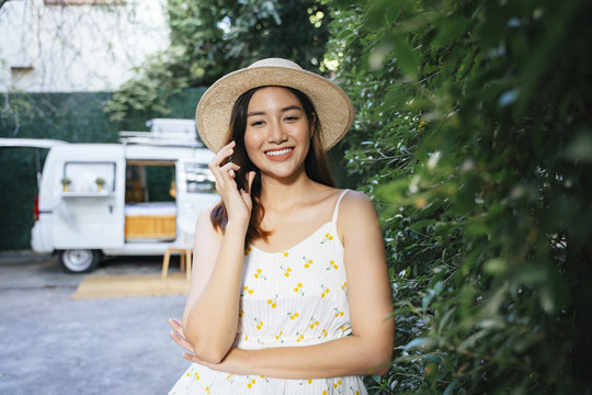 美丽的亚洲女游客戴着帽子，穿着白色衣服在公园里打电话。