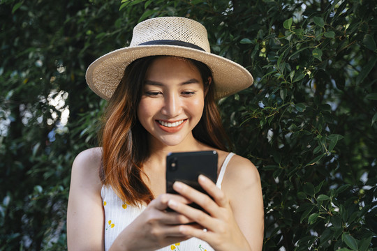 快乐快乐的亚洲女人戴着帽子在户外与智能手机聊天。