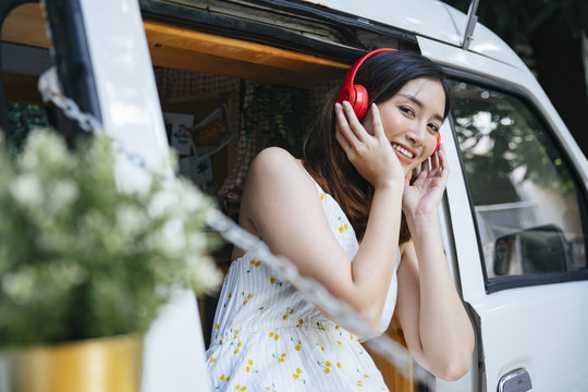 穿着白色连衣裙的美丽亚洲女性在CV车上用无线耳机听音乐。