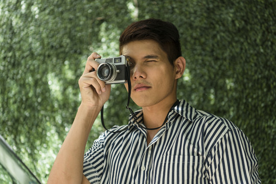 初学摄影的亚洲摄影师在公园尝试使用复古胶卷相机的肖像。