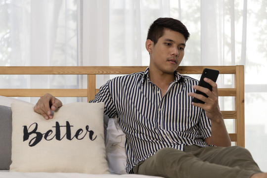 亚洲男人在家里卧室里使用智能手机。