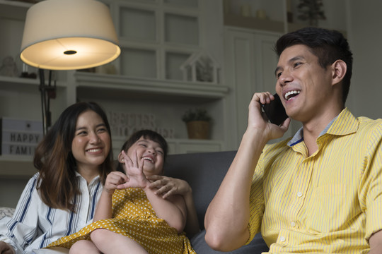 亚洲家庭在家里共度时光。爸爸在打电话。母亲和女儿看着父亲。