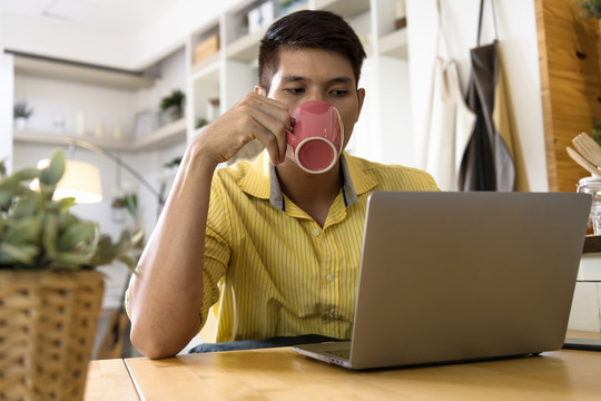 亚洲商人一边喝咖啡一边看笔记本电脑。