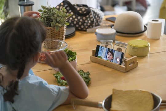 孩子在厨房餐桌上用智能手机做饭。