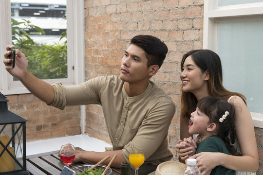 亚洲家庭在餐厅吃午饭时用智能手机自拍。
