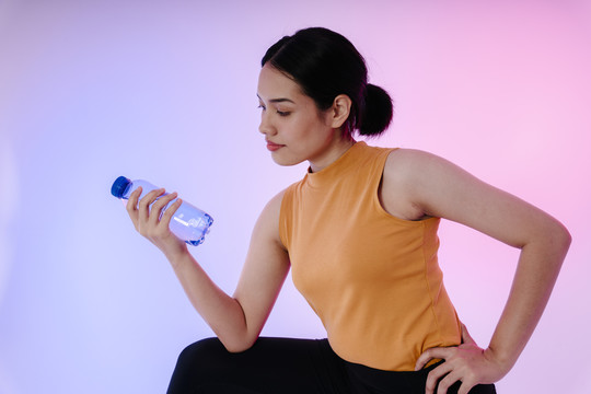 一位年轻的运动健康的亚洲女性的肖像画，在柔和的背景下用一瓶水隔离。