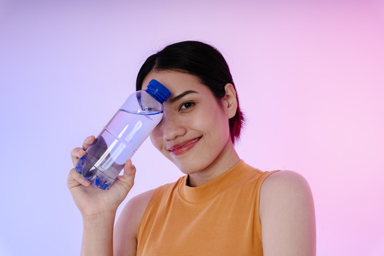 一位年轻的运动健康的亚洲女性的肖像画，在柔和的背景下用一瓶水隔离。