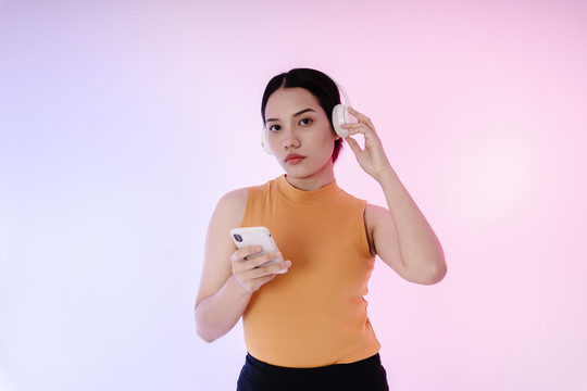 运动型亚洲女性的肖像，戴着耳机和智能手机听音乐。