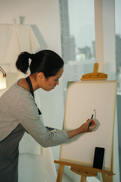 后视图-专业女艺术家在画布上使用毛笔绘画。画架模型。