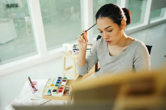 画室里年轻的亚洲女艺术家在画布上绘画的肖像。