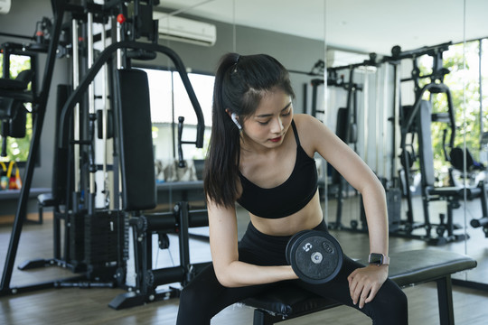 健康的亚洲女性在健身房练习哑铃和听音乐。