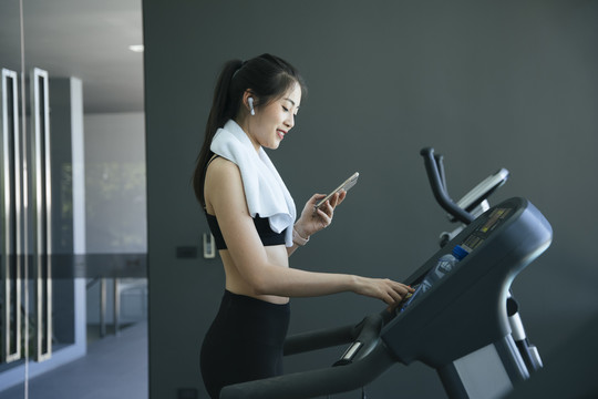 健康的亚洲女性在跑步机上锻炼时在智能手机上选择流媒体歌曲。