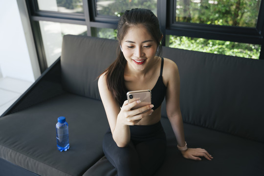 健康的亚洲女性在家锻炼后，用智能手机在沙发上放松。