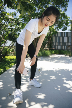 穿着白衬衫的健康亚洲女性在公园锻炼前热身的照片。