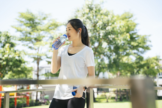 健康的亚洲女性在公园锻炼后饮用瓶装水。