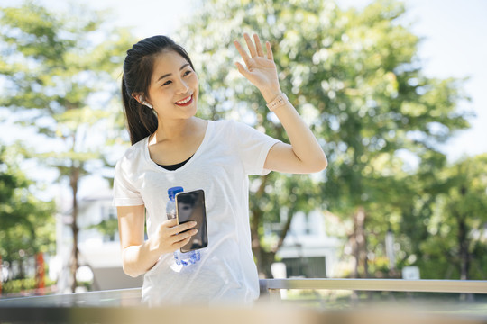 在公园里，一位健康的亚洲女性挥手向朋友问好。
