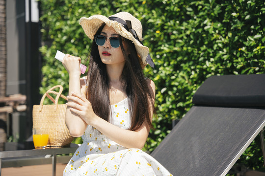 夏季，亚洲旅行妇女在户外涂抹防晒霜。