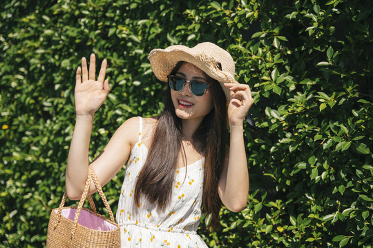 在自然背景下，一位美丽的亚洲旅行者戴着帽子和太阳镜。