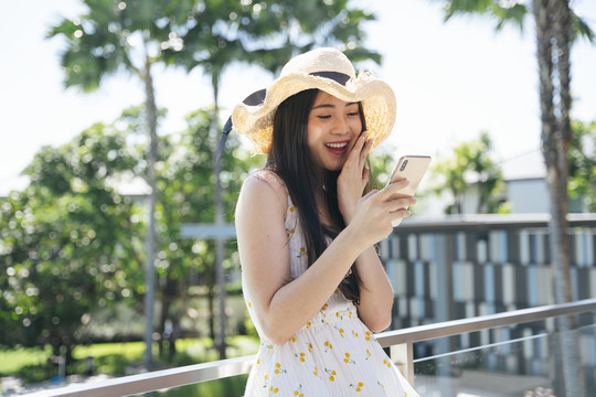 美丽的亚洲女旅行者在酒店阳台上戴着智能手机的帽子。