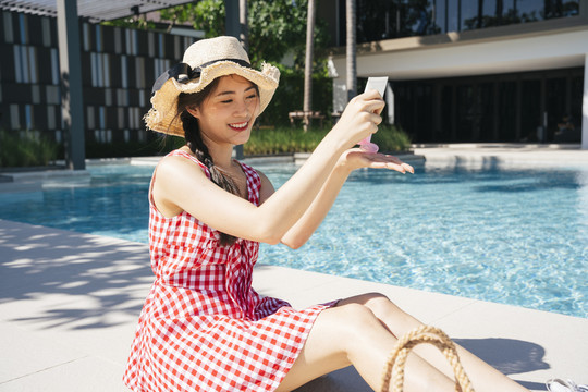 美丽的亚洲女人穿着粉红色的裙子，在游泳池附近涂防晒霜。