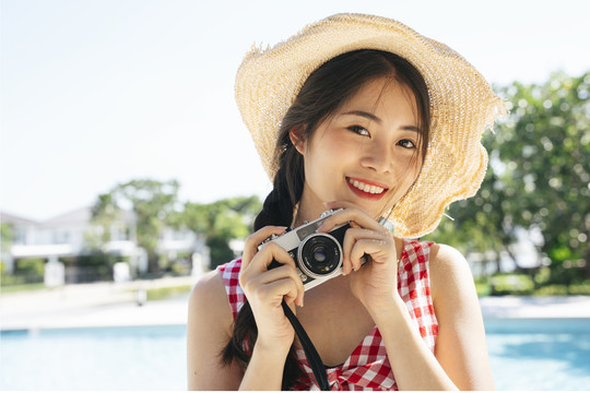 美丽的亚洲女人戴着帽子用相机拍照的肖像。