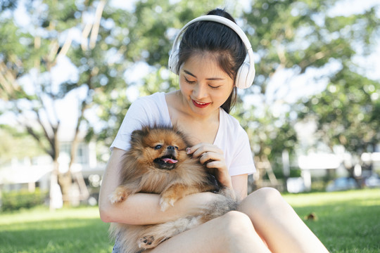 在公园里，主人戴着耳机和波美拉尼亚斯皮茨犬。