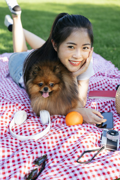 公园垫子上的亚洲女人和狗的肖像。和可爱的宠物野餐。