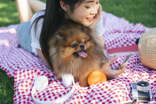 公园垫子上的亚洲女人和狗的肖像。和可爱的宠物野餐。