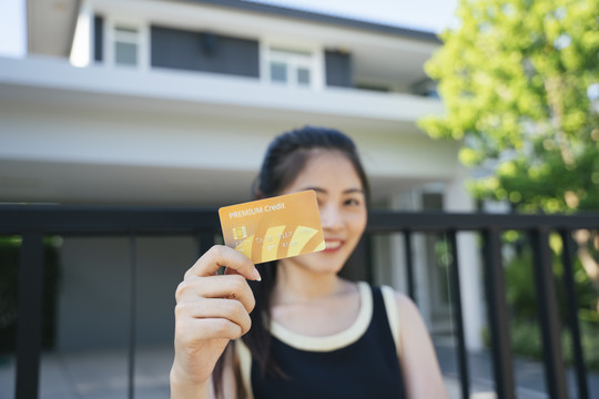 美丽的亚洲女人在豪宅前用信用卡。购买地产的概念。