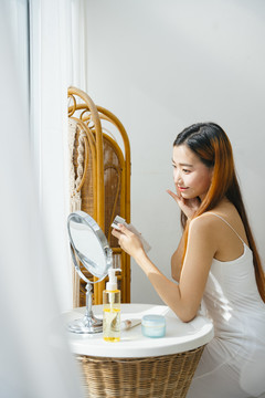美丽的年轻亚洲女人在家里对着镜子化妆。